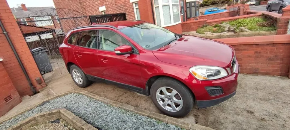Red SUV parked in residential driveway with brick buildings and walls visible