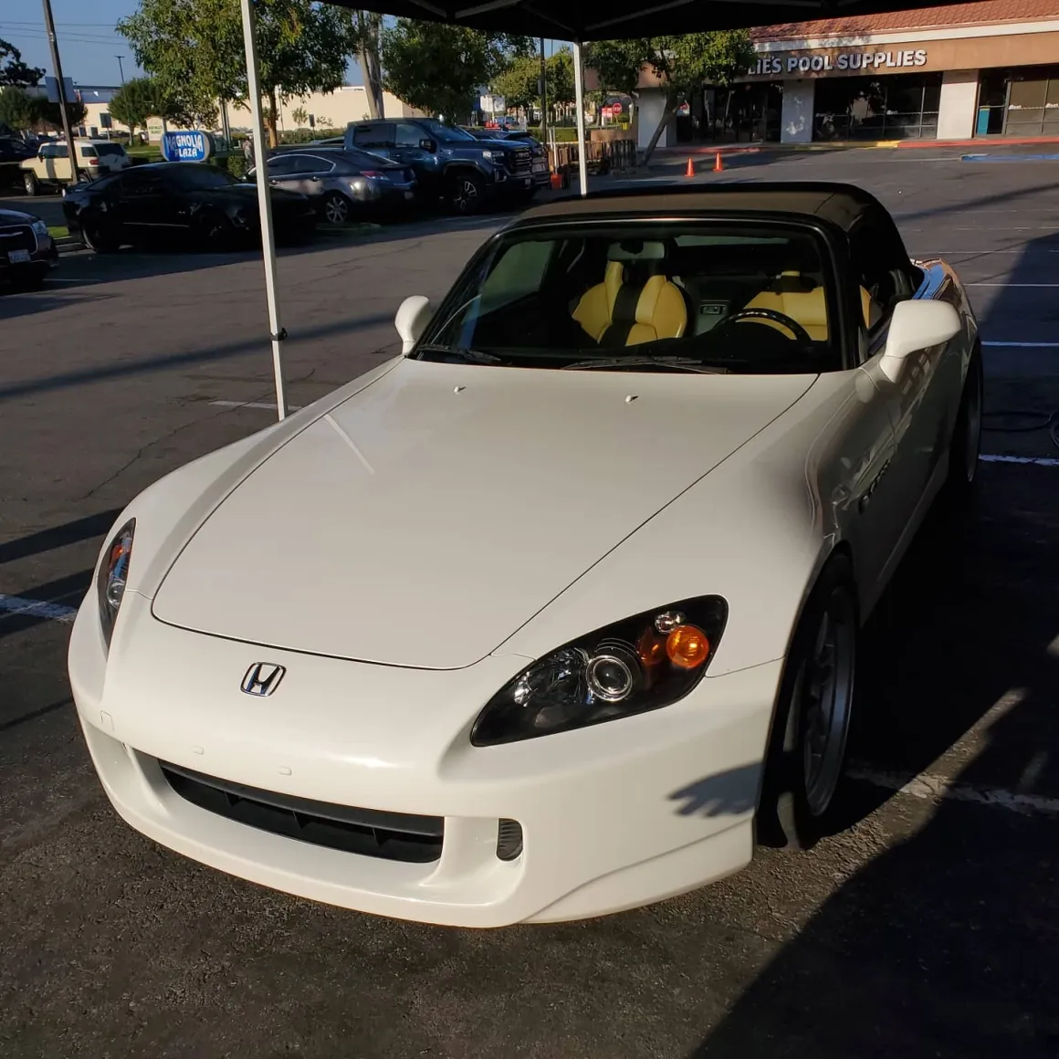White Honda S2000 convertible with yellow interior parked in shopping center lot
