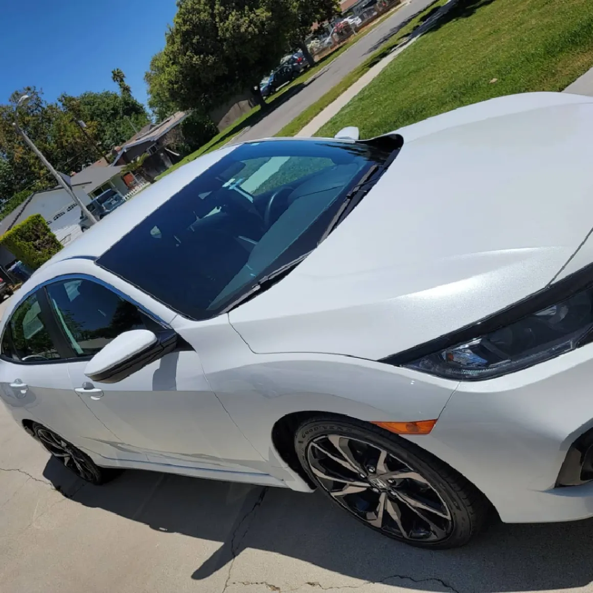 White sports car parked in driveway with open hatchback on sunny day