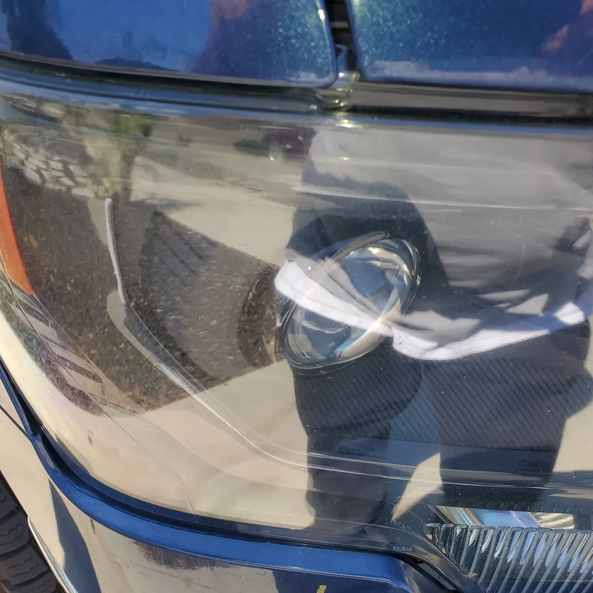 Close-up of car headlight with white tape repair on blue vehicle hood