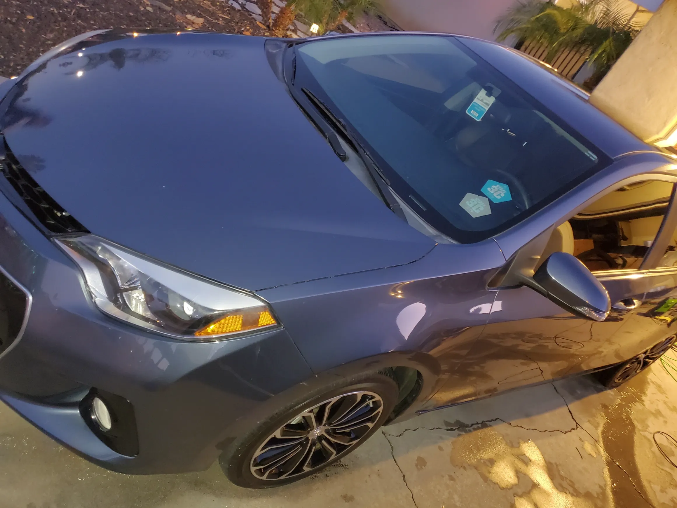 Blue compact car parked in driveway at dusk with sunshade on windshield