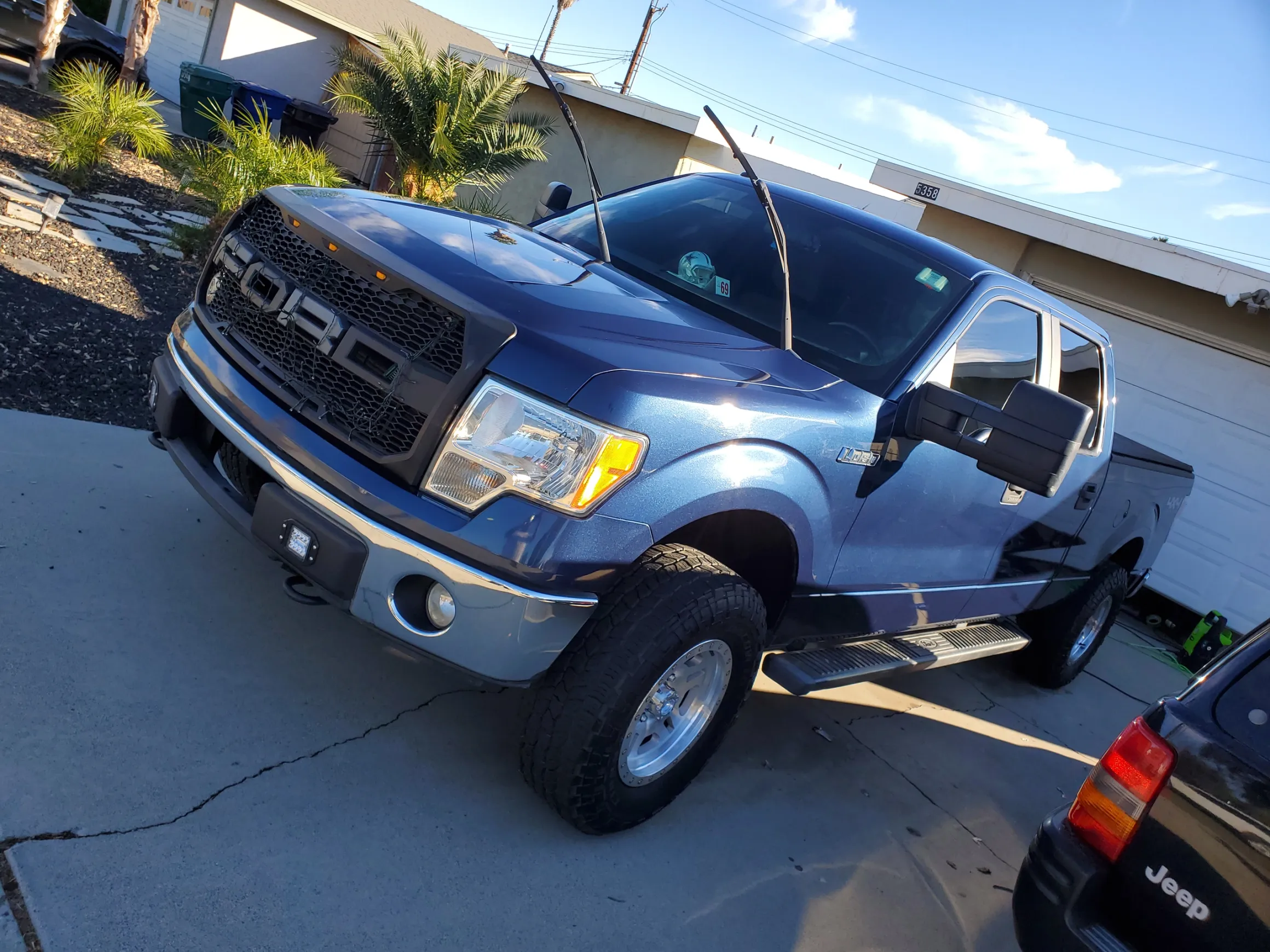 Blue Ford pickup truck with extended cab parked in driveway near palm trees