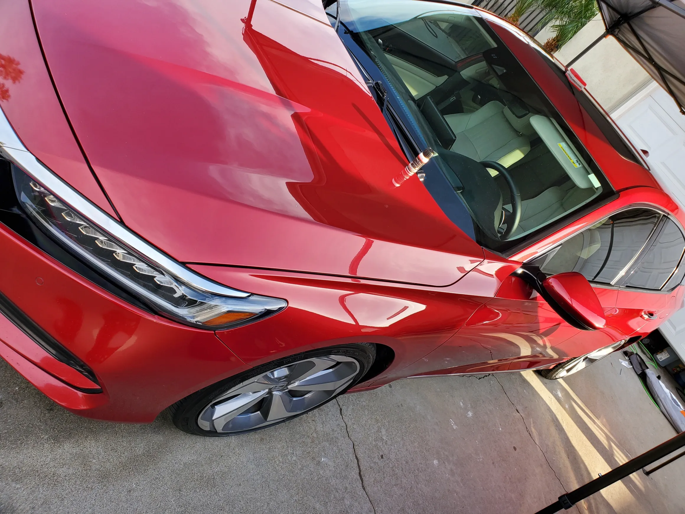 Red sedan parked in driveway with open driver door and pink vehicle visible in background