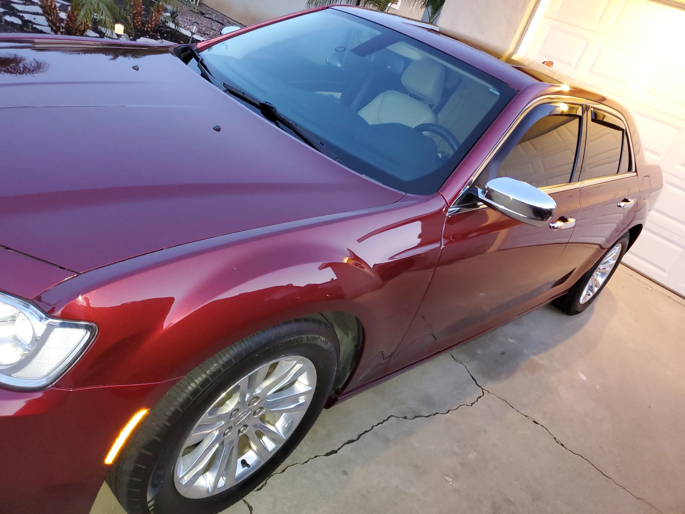 Red sedan parked in driveway with chrome mirror and alloy wheels visible