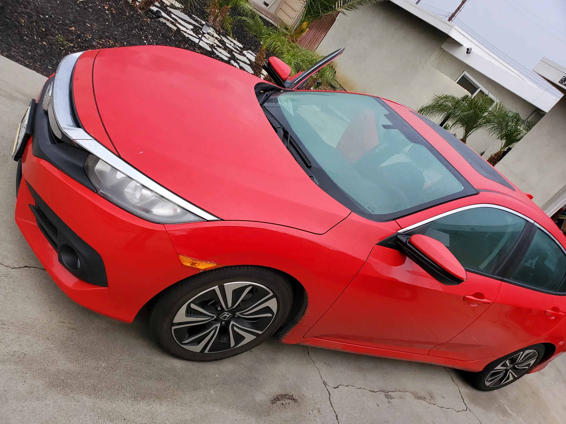 Red Honda Civic parked in driveway with car cover partially on hood