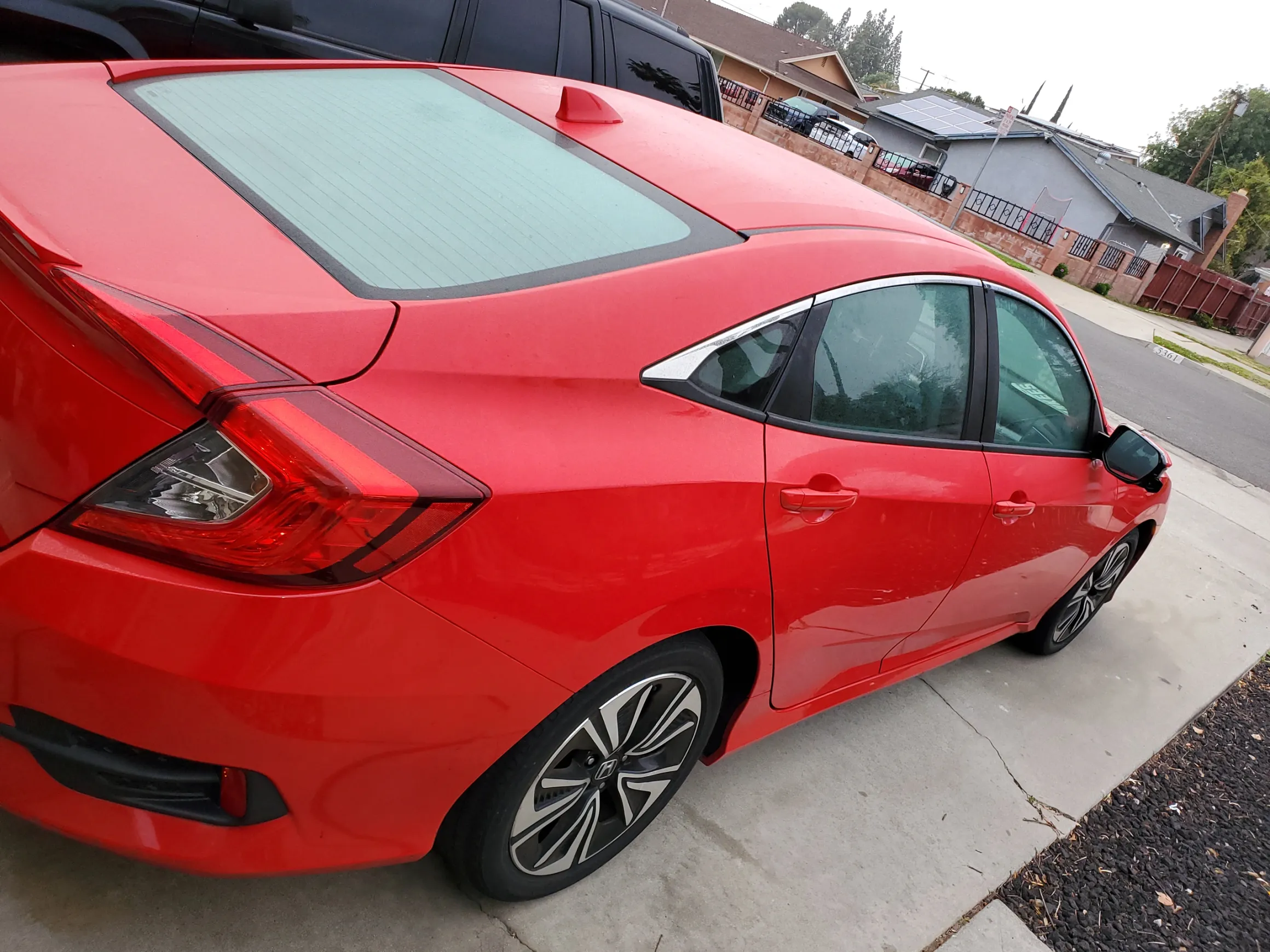 Bright red compact sedan parked on residential driveway with sunshade on windshield