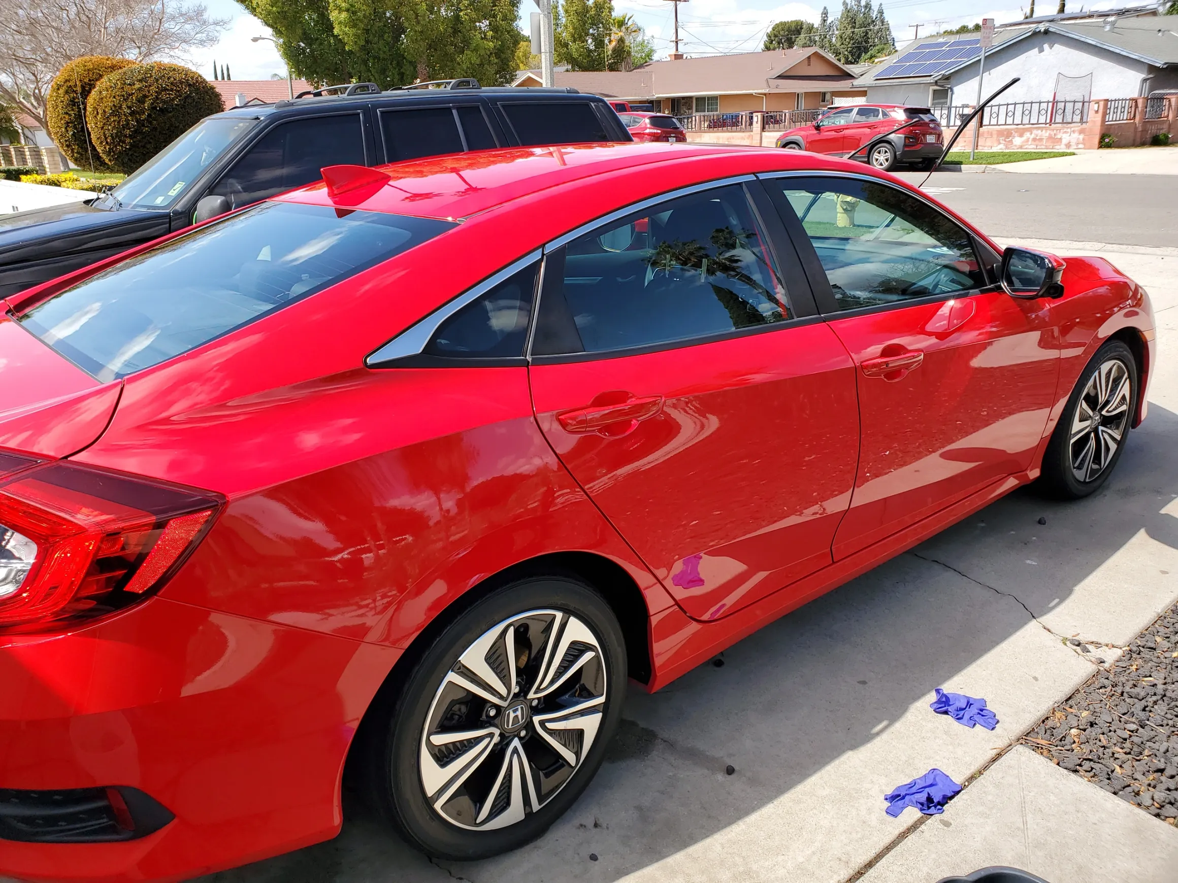 Red Honda Civic parked on residential street with blue paw print stickers on curb