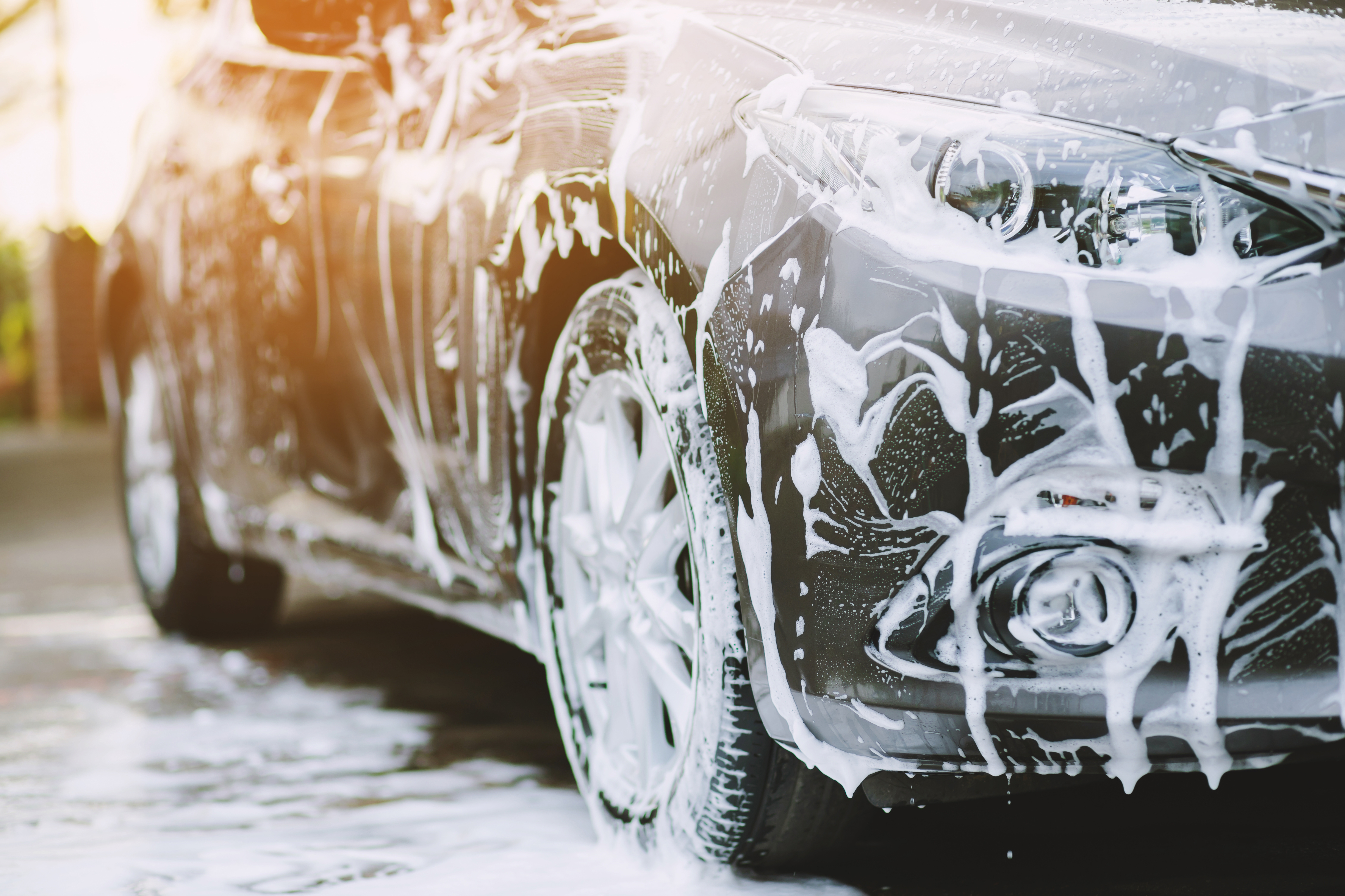 Cars covered in white foam during an outdoor wash station cleaning service