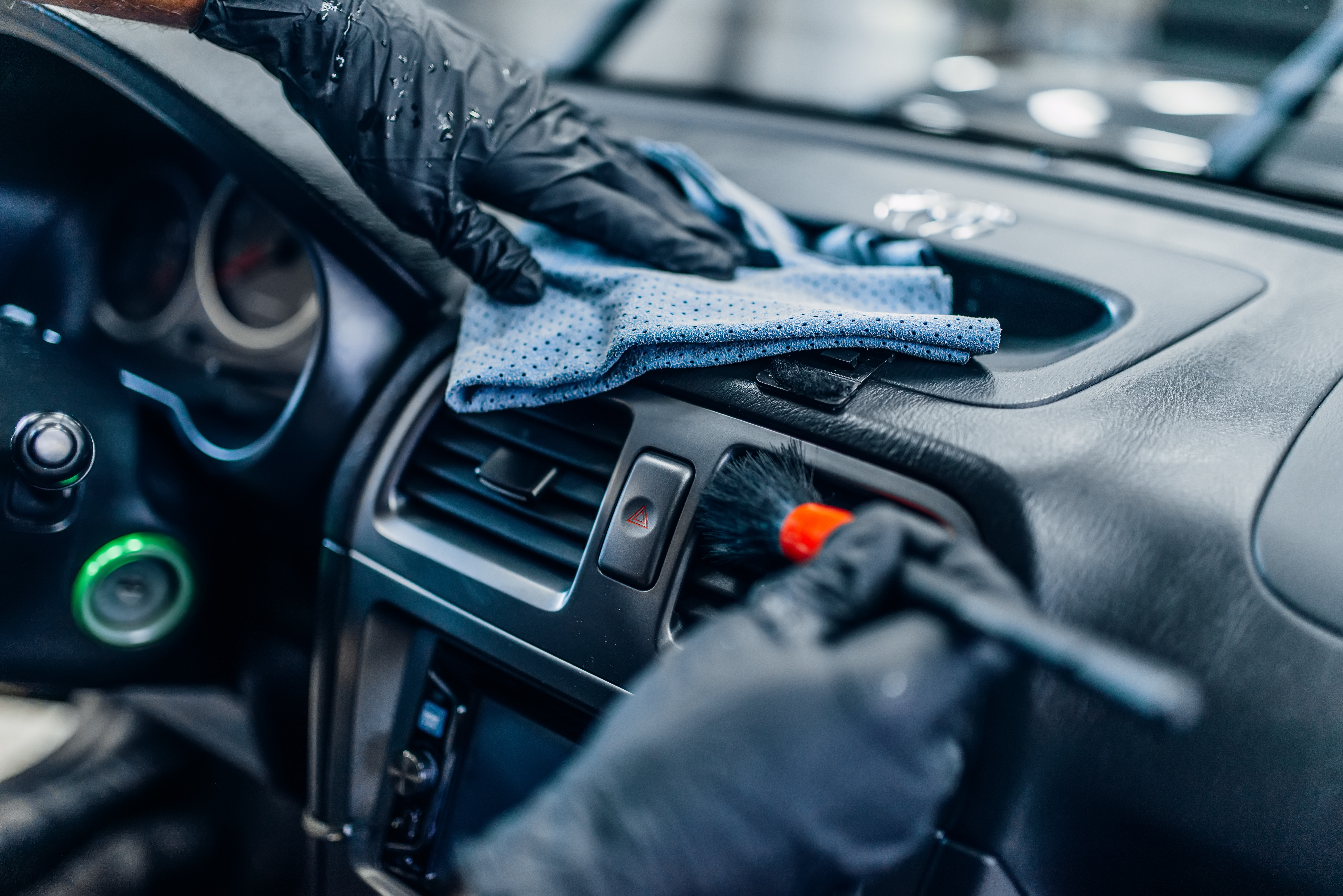 Person wearing black gloves cleaning car dashboard with blue microfiber cloth