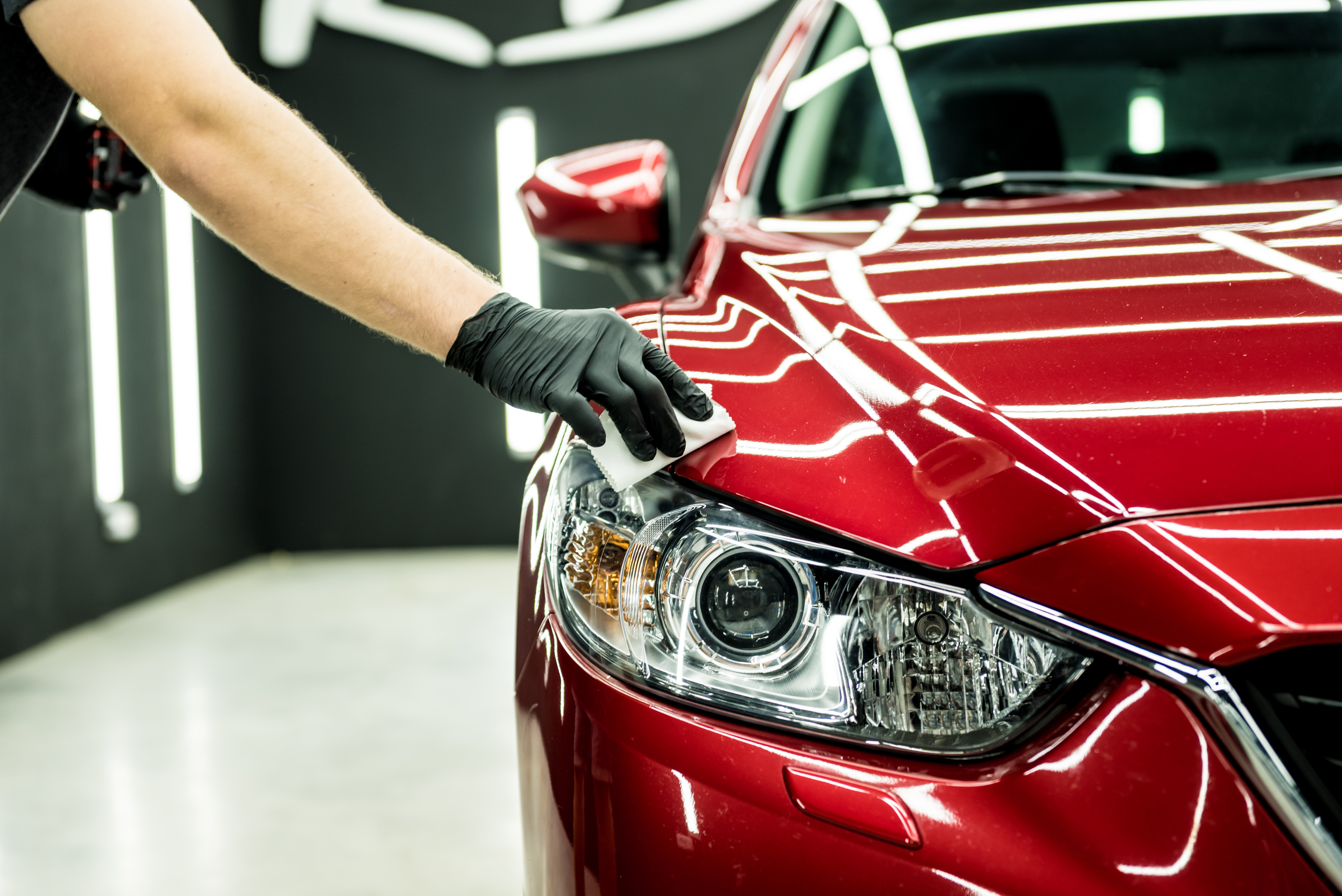 Professional detailer polishing red car hood with microfiber cloth in bright garage
